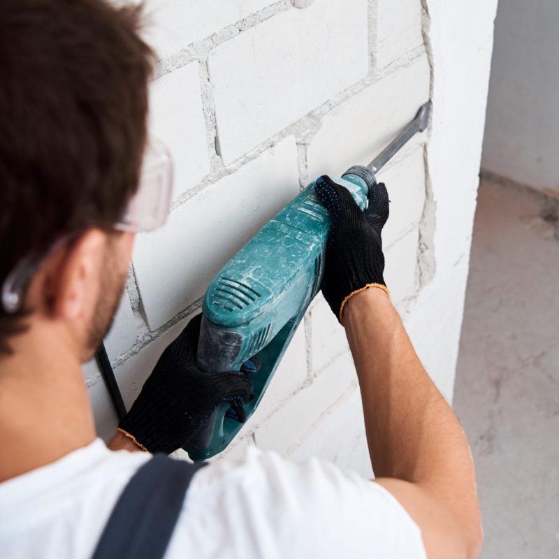 Renovation concept. Man with demolition hammer remove stucco from wall